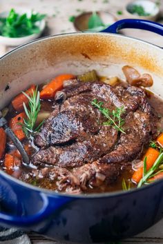 a pot filled with beef and carrots on top of a wooden table next to other dishes