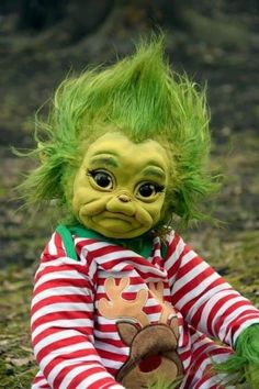 a troll doll with green hair sitting on the ground wearing a red and white striped shirt