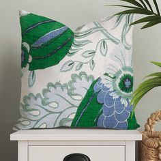 a green and blue pillow sitting on top of a white table next to a potted plant