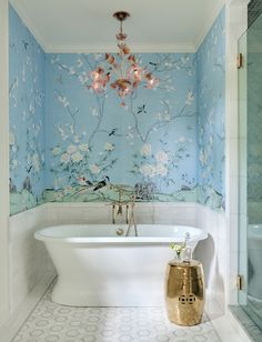 a white bath tub sitting under a chandelier next to a wall mounted mirror