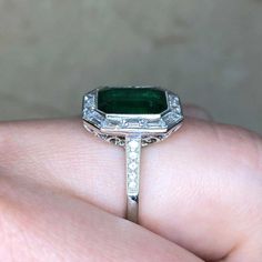 a woman's hand holding an emerald and diamond ring