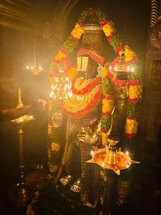 a statue with candles and flowers around it in a dark room next to a lamp