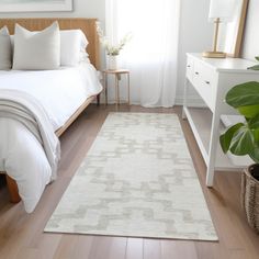 a bedroom with white bedding and wooden flooring next to a large green plant