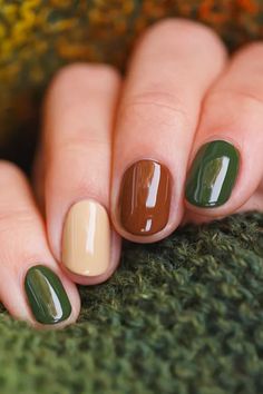 A close-up of a hand with different fall nail polish colors, including brown, cream white, and olive green.