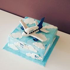 a cake shaped like an airplane on top of a blue and white box with clouds