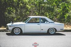 an old white car parked on the side of the road in front of some trees