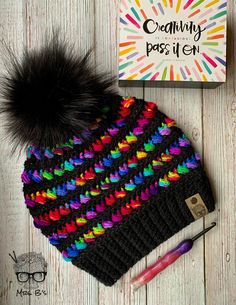 a crocheted hat with a pom - pom sits next to a book