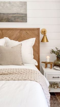 a bed with white linens and pillows in a small room next to a painting on the wall