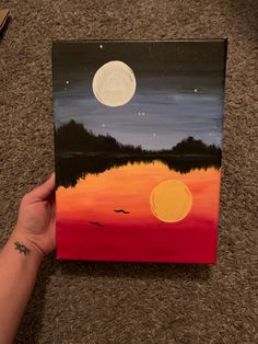 someone is holding up a painting on the floor with a full moon in the sky