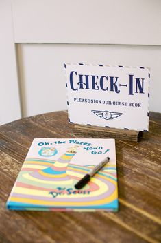 a check - in sign sitting on top of a wooden table next to a notebook