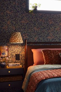 a bed sitting under a window next to a nightstand with a lamp on top of it