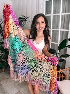 a woman holding up a colorful crocheted shawl