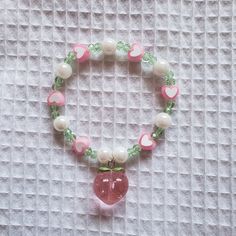 This peach blossom bracelet was inspired by the reason I look forward to summer every year - peaches! It features a delightful combination of green and pink, with pearls and a peach charm! Materials: - 0.7 mm elastic string - green beads - pink heart beads - pearl beads - pink peach charm Elastic Bracelets, Peach Bracelet, Peach Necklace, Pink Pearl Bracelet, Blossom Bracelet, Crystal Bead Jewelry, Fancy Beads, Bead Charms Diy, Crochet Design Pattern