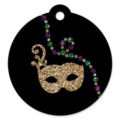 a black round ornament with a mask and beads on the front, in gold glitter