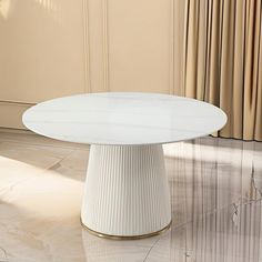 a round white table with gold trim on the base in front of a beige wall