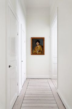 an empty white hallway with a painting on the wall