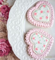 two decorated cookies sitting on top of a white plate next to pink and green flowers