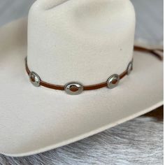 This hat band is made with brown leather that is laced through silver oval conchos. It is adjustable in the back with a metal slide. Made in the USA 1 1/8" x 7/8" conchos Genuine leather *This product is for 1 single hat band. Hat not included. Southwestern Concho Hat For Rodeo, Southwestern Style Concho Hat For Rodeo, Adjustable Brown Hat Band For Flat Crown, Adjustable Brown Country Style Hat Bands, Vintage Adjustable Leather Hat Bands, Adjustable Leather Vintage Hat Bands, Adjustable Vintage Leather Hat Bands, Vintage Adjustable Hat Bands For Rodeo, Adjustable Vintage Hat Bands For Rodeo