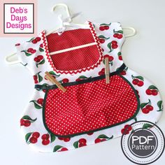 two aprons with cherries on them are hanging from clothes pins and one has a red polka dot design