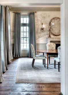 a dining room with chairs and a table in front of a window that has drapes on it