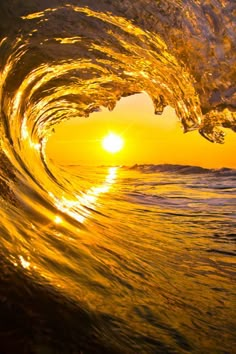 an ocean wave with the sun setting in the background