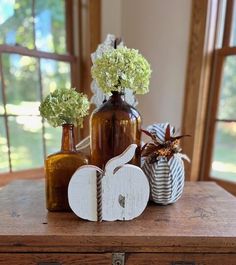 three vases with flowers in them sitting on a table next to an old trunk