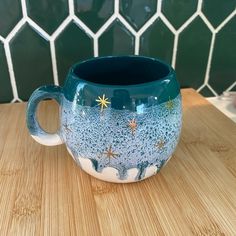 a blue and white mug sitting on top of a wooden table next to a tiled wall