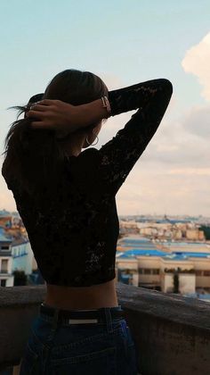 a woman standing on top of a roof with her hands behind her head and looking at the sky