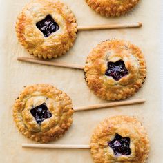 four blueberry pies sitting on top of a piece of parchment paper with toothpicks