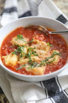 a white bowl filled with pasta and tomato soup on top of a towel next to a spoon