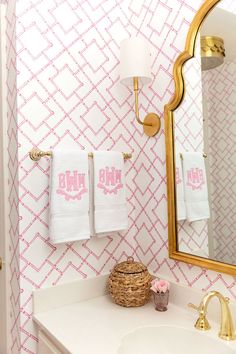 a bathroom with pink and white wallpaper, gold mirror and two towels on the rack