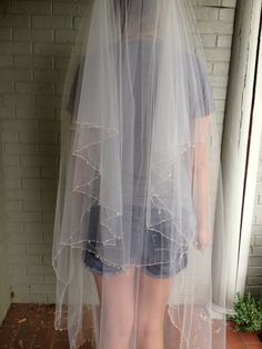 a woman standing in front of a brick wall wearing a veil