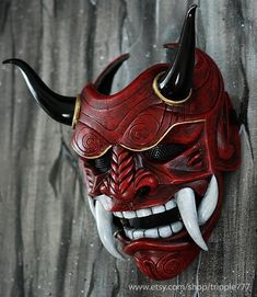 a red mask with horns and fangs on it's face is hanging from the wall