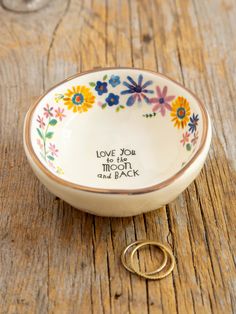 a small white bowl with flowers on it and a gold ring sitting next to it