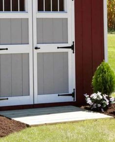 a red and white shed with two doors on the outside, and flowers in the front