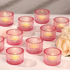 many pink glass cups with candles in them on a table next to a white rose