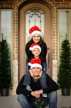 a family poses for a christmas photo in front of their house with santa hats on