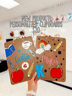 a person holding up two brown clipboards with school related stickers on them and the words new product, personalized clipboards