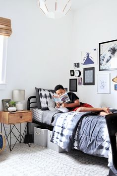 a young boy laying in his bed reading a book while sitting on the edge of the bed