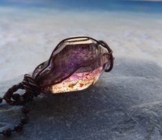 Stunning double terminated Phantom Amethyst Crystal from the Mwana Lubaba Mine in Zambia is a rare stone combining smoky quartz and amethyst. The crystal formation has rich interior patterns with red hematite inclusions. Formed over millions of years sustaining changes in molten temperatures and tectonic movement within the earth, this crystal is in its natural rough form, not cut or polished in any way.  The crystal  is simply wire wrapped and strung on an oxidized copper ball chain 27" long. (Note: prop does not show true length of chain) Stone size is  1 1/8" long and 5/8' at the widest point.  Phantom crystals are named for the crystal formations which float from within the stone giving it a double crystal appearance.  Note: oxidized metal finishes are more sensitive to salt water, per Handmade Amethyst Crystals For Meditation, Purple Spiritual Crystals For Jewelry Making, Handmade Lavender Crystals For Spiritual Use, Handmade Lavender Spiritual Crystals, Large Purple Stone Crystals As Gift, Handmade Mystical Amethyst Crystals, Handmade Mystical Purple Crystals, Handmade Lavender Amethyst Crystals, Bohemian Purple Amethyst Crystals