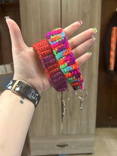 a hand holding two multicolored knitted bracelets on it's fingers