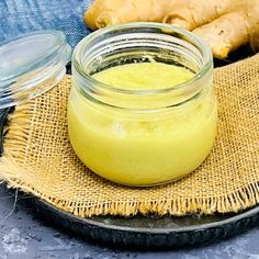 a jar filled with yellow liquid sitting on top of a table next to sliced ginger