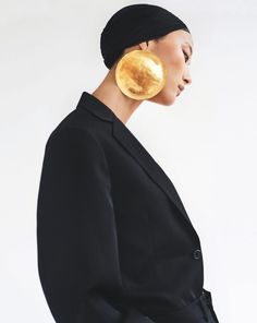 a woman wearing a black jacket and gold earring on top of her head in front of a white background