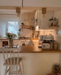 a kitchen with white cabinets and wooden counter top next to a bar stool in front of a window