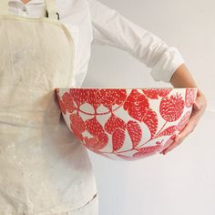 a woman in an apron holding a red and white bowl with flowers on the bottom