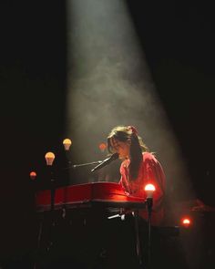 a woman sitting at a red piano in front of a microphone on stage with lights behind her