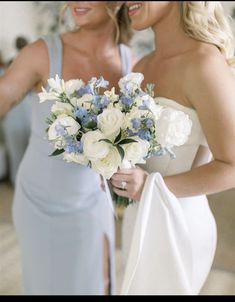 two beautiful women standing next to each other holding bouquets