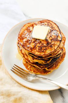 a stack of pancakes with butter on top and a fork next to it, sitting on a white plate