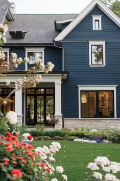 a blue house with white trim and flowers in the front yard on a sunny day