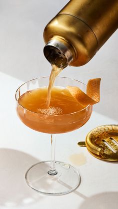 an orange drink being poured into a martini glass with gold garnishes on the rim